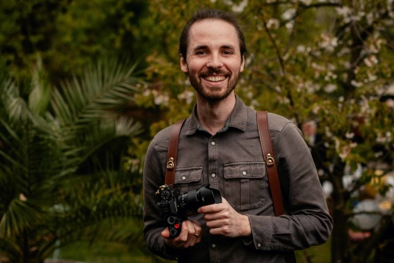 Hochzeitsfotograf Kevin Kurek lächelt in die Kamera und hält eine Kamera in der Hand.
