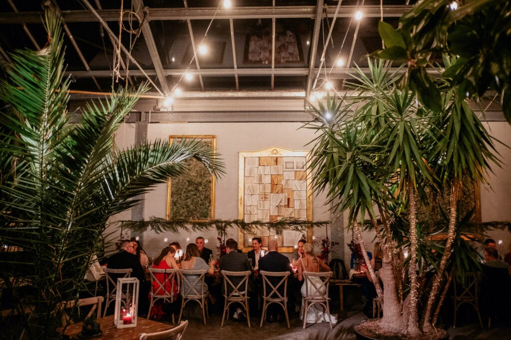 Hochzeitsgäste sitzen zwischen großen Palmen im Palmencafé an einem großen Tisch und warten auf das Essen.
